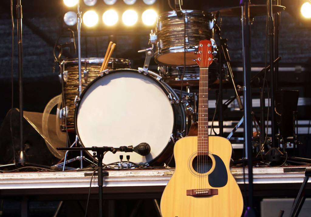 Acoustic guitar resting near a drum set on stage.