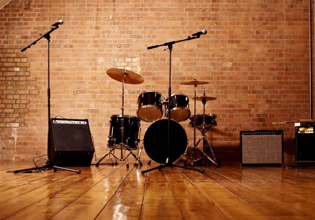 A drum set and microphones set up on a wooden floor against a brick wall.