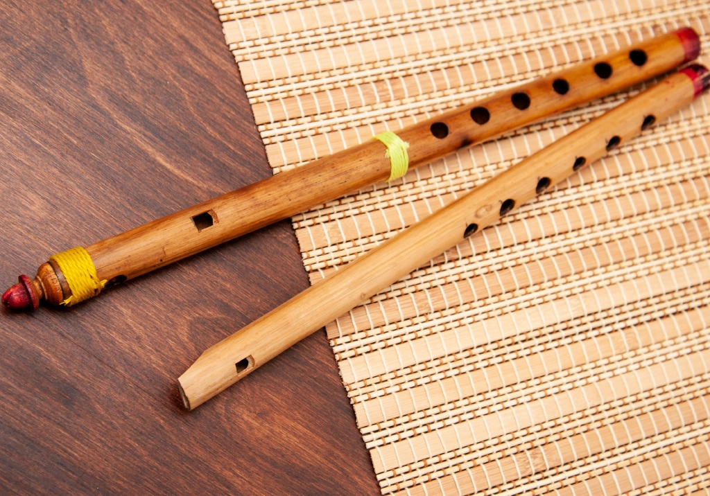 Two wooden flutes placed on a woven mat and wooden surface.