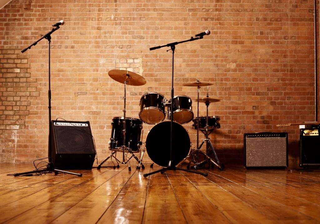 A drum set and microphones set up on a wooden floor against a brick wall.
